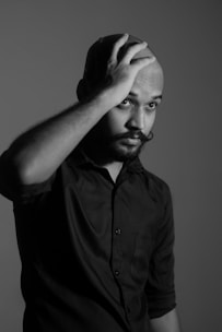 Close-up of a man touching his patchy beard thoughtfully against a dark background.