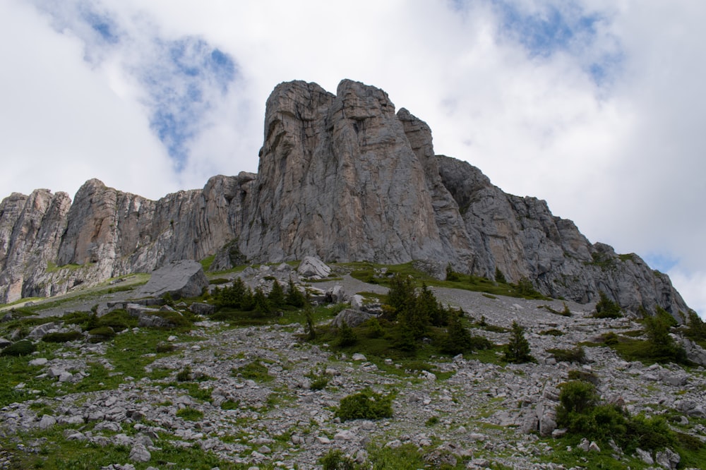 green grass field near gray rock formation under white clouds during daytime