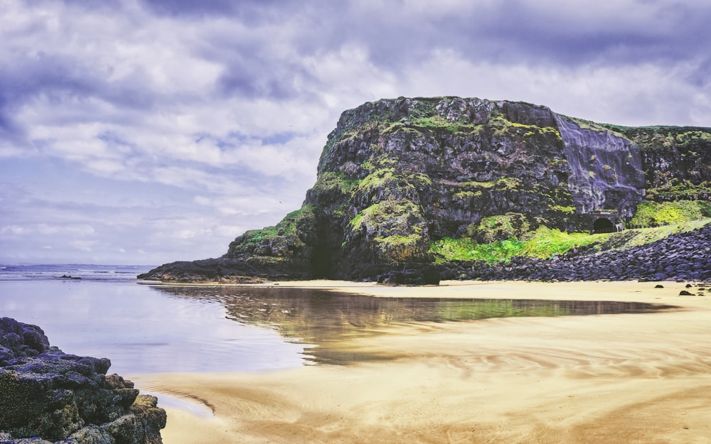 green and brown rock formation on sea shore under white clouds and blue sky during daytime