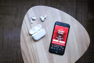 black android smartphone beside white earbuds on brown wooden table