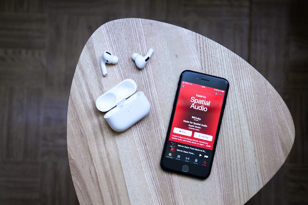 black android smartphone beside white earbuds on brown wooden table