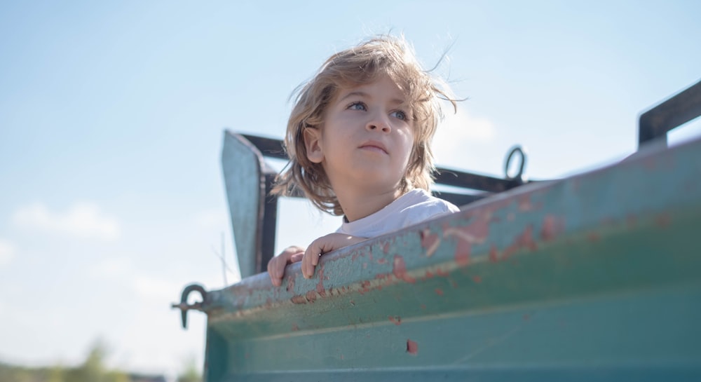 girl in white and pink shirt on green metal boat during daytime