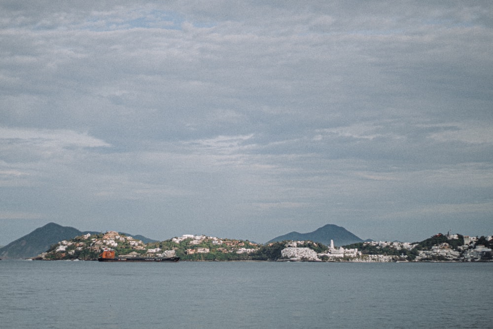 white and green mountain near body of water under white clouds during daytime