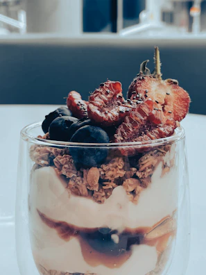 A tall glass filled with layered strawberry parfait topped with fresh berries and mint.