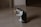 A black and white cat is sitting on a wooden floor, playing with a toy attached to a string. The toy appears to be a small stuffed animal with a yellow leaf-like attachment. The cat is engaging with the toy, using its front paws and mouth.