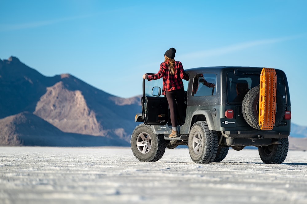 man in red jacket and black pants sitting on black jeep wrangler