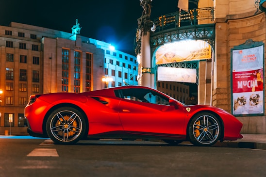 A gleaming red exotic sports car parked on a city street at sunset, reflecting the vibrant urban lights.