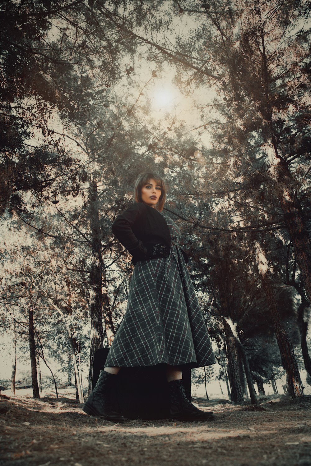 woman in black and white plaid dress standing under trees during daytime