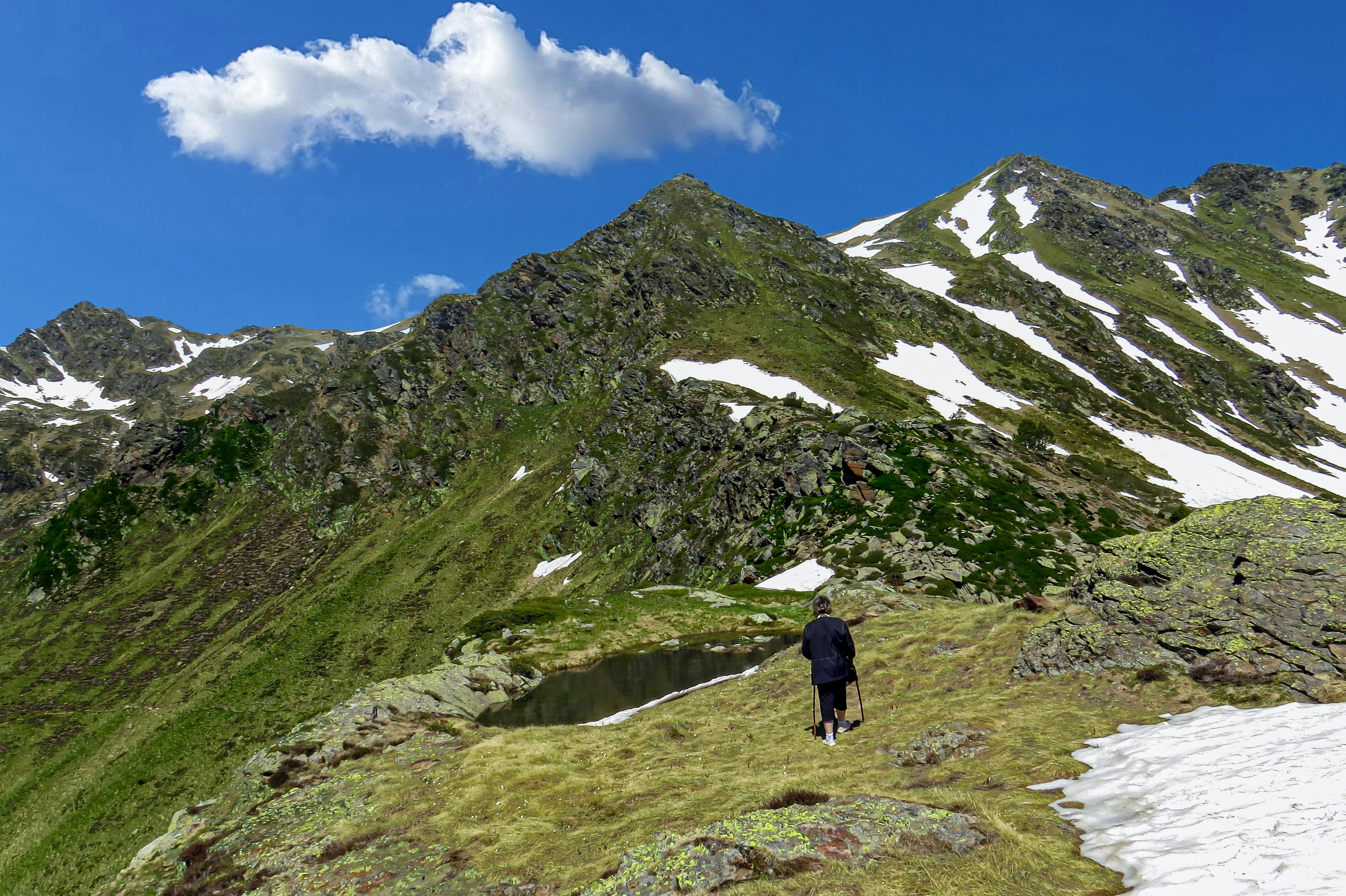 person in black jacket walking on green grass field near mountain under blue sky during daytime