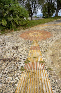 Patterned ceramic tiles creating a vibrant walkway through a sunny backyard.