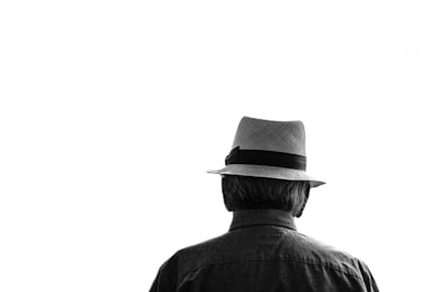 A sleek black fedora displayed on a minimalist white stand against a soft background.