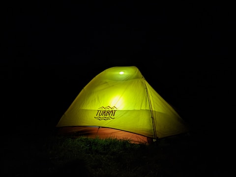 A bright yellow tent illuminated from within, set against a dark background, creating a contrast that highlights the tent's outline.