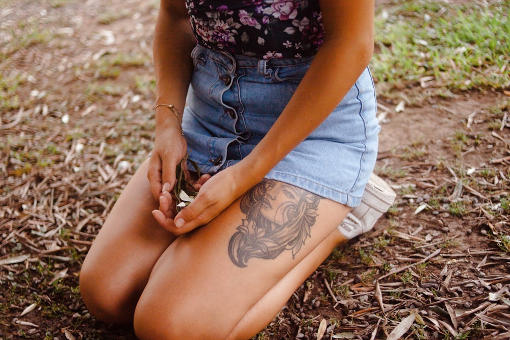 woman in blue denim shorts and black floral tank top sitting on ground