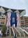 The image depicts a large, modern building with a prominent display of the Union Jack flag across its central columns. There is an extensive staircase leading up to the entrance, adorned with pink flower arrangements. Several people are present, some holding umbrellas, indicating that it might be raining.