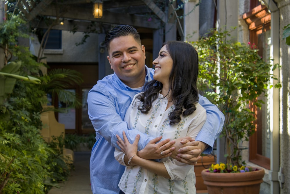 man in blue dress shirt hugging woman in white long sleeve shirt