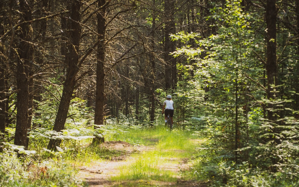 man in white shirt walking on dirt road between trees during daytime