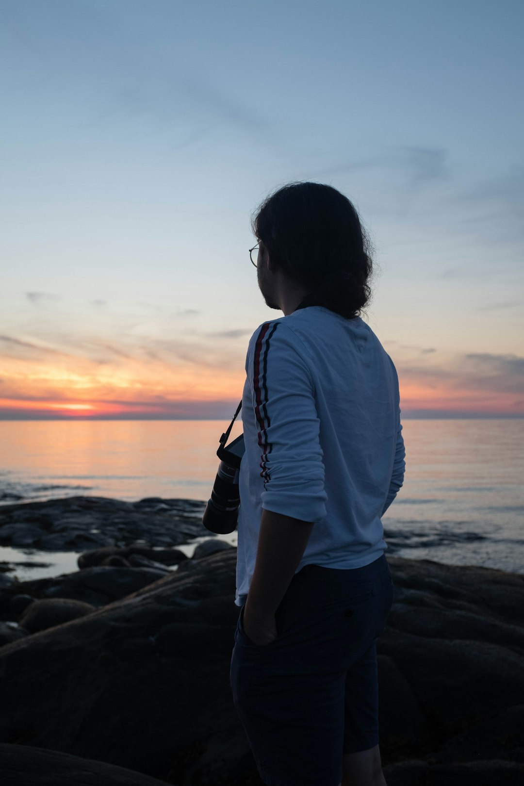 woman in white long sleeve shirt standing on rocky shore during sunset