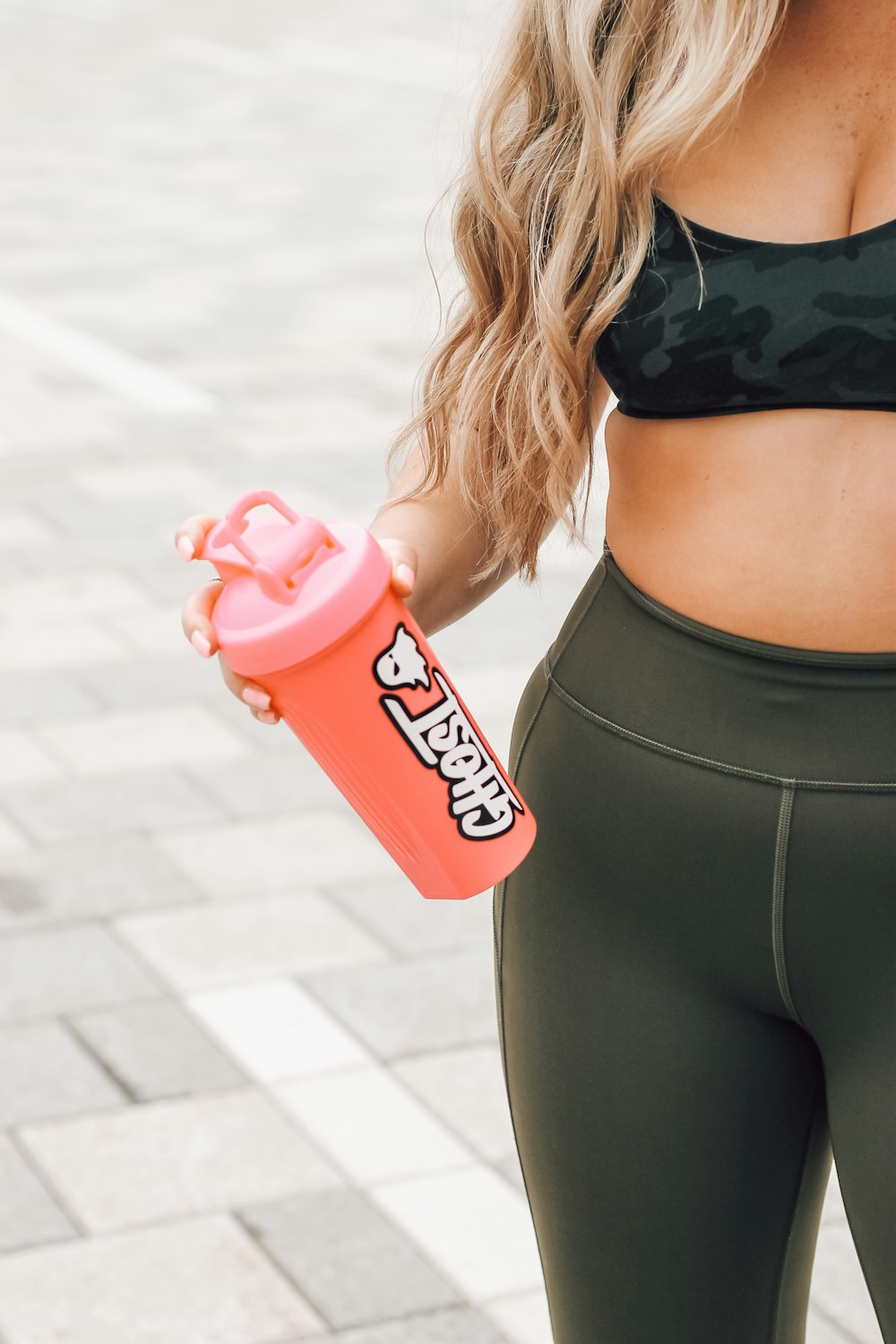 woman in black bra and black leggings holding red and white plastic bottle