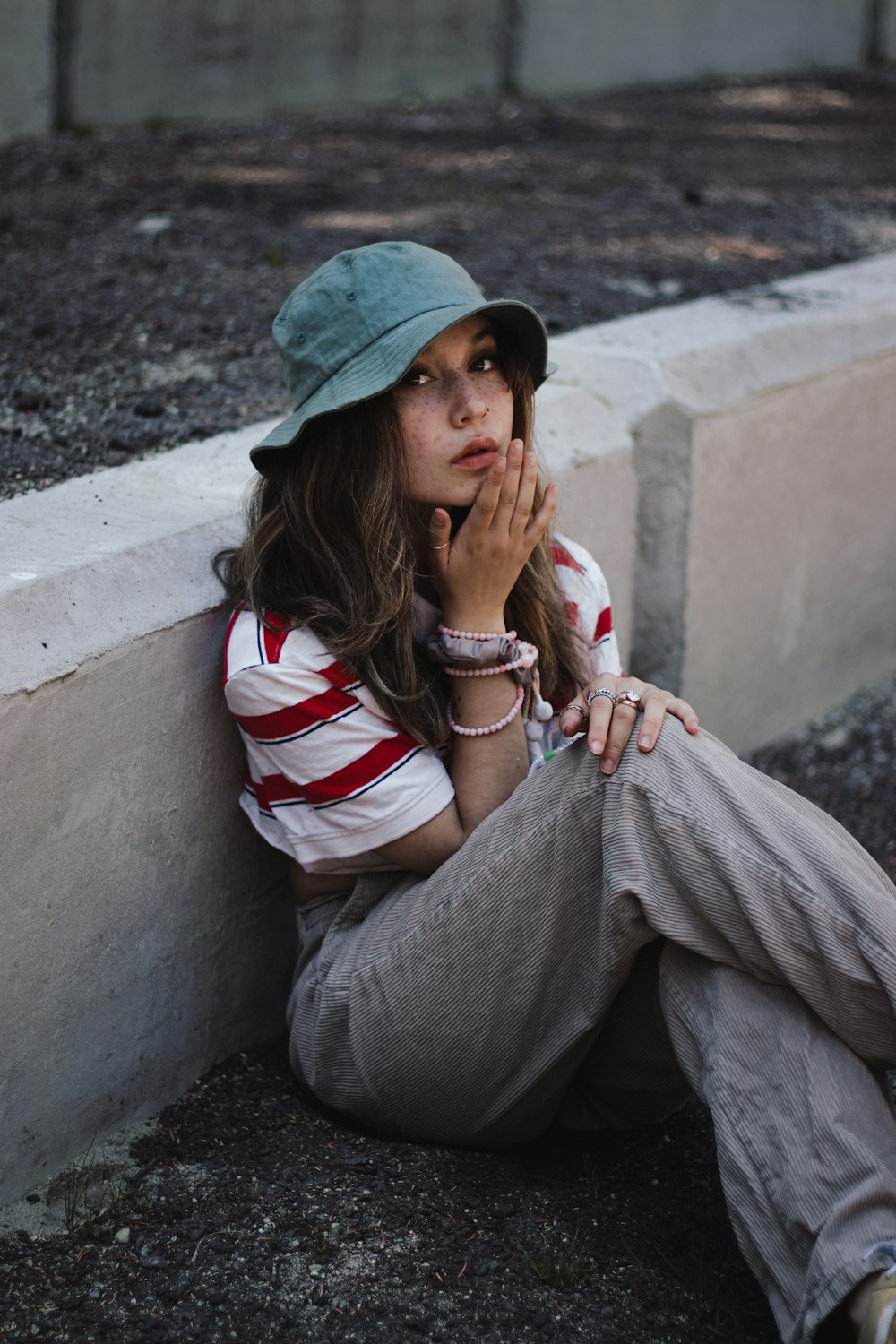 woman in white red and blue striped long sleeve shirt and gray pants sitting on concrete