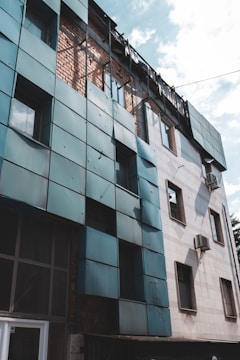 A partially destroyed building with exposed brick and damaged metal panels. The sky is visible above, and air conditioning units are attached to the walls.