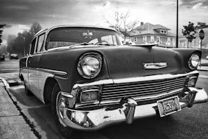 A black and white photo of a vintage car parked outside a grand estate.