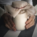 Hands holding a small jar of rich cream with a soft natural background.