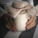Hands gently holding a small jar of cream surrounded by natural ingredients.