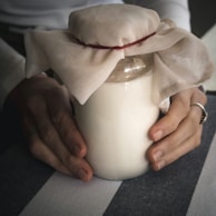 Hands gently holding a jar of leafhea cream surrounded by fresh herbs.