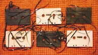 Several vintage audio cassette tapes are displayed on a textured orange surface. The tapes are intermingled with unwound, tangled magnetic tape, creating a chaotic yet nostalgic arrangement. The contrast between black and white cassettes adds visual interest.