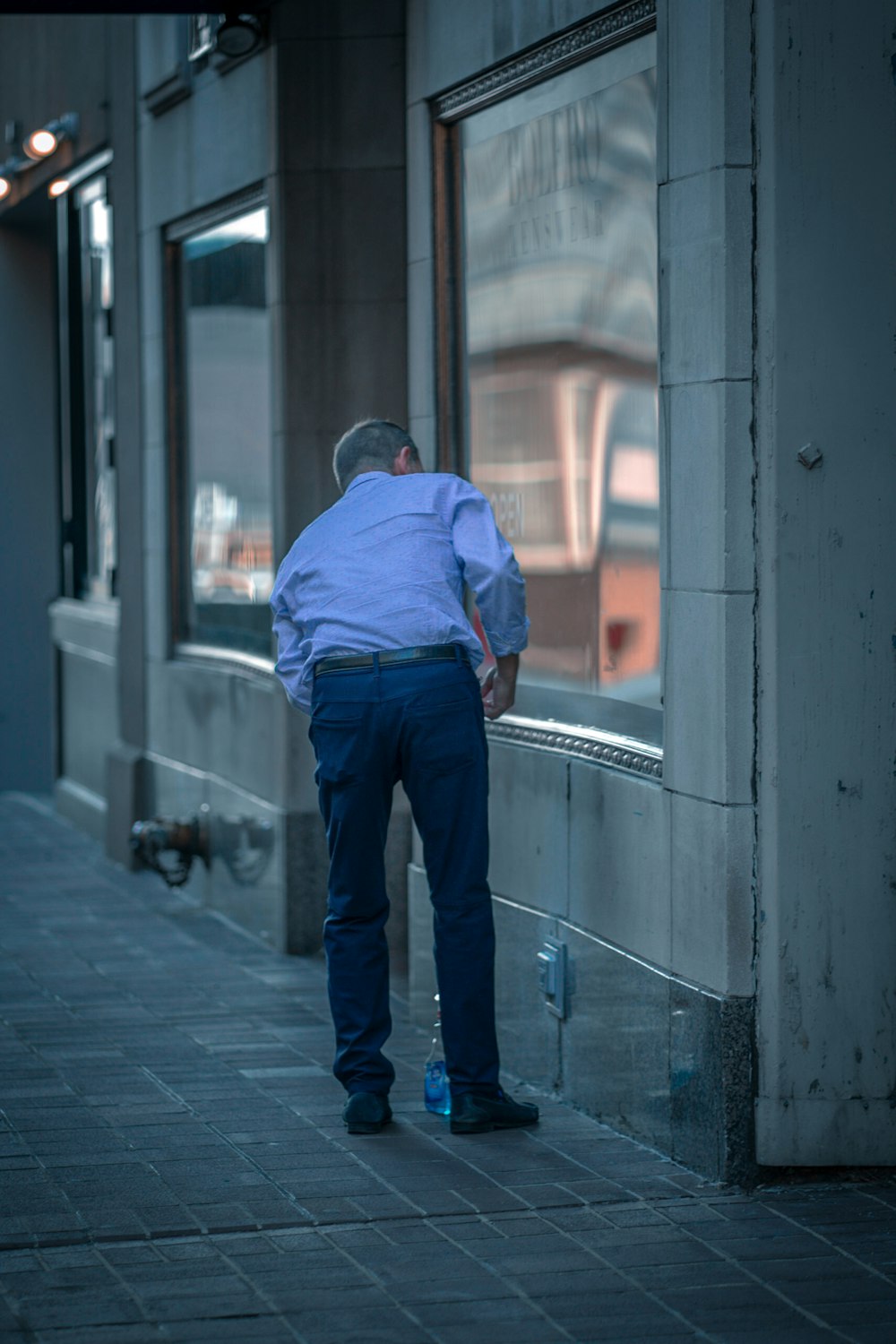 man in blue dress shirt and blue denim jeans standing on gray concrete floor