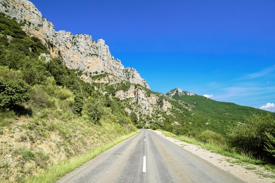 gray asphalt road between green grass field and gray rocky mountain under blue sky during daytime