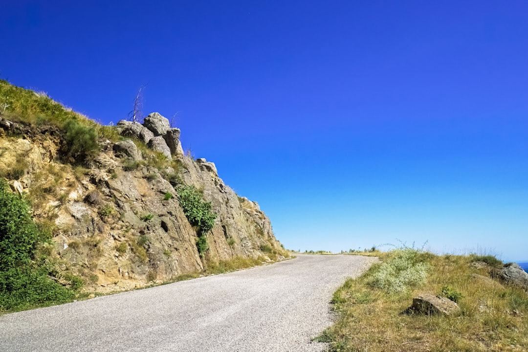 gray asphalt road between green grass covered hill under blue sky during daytime