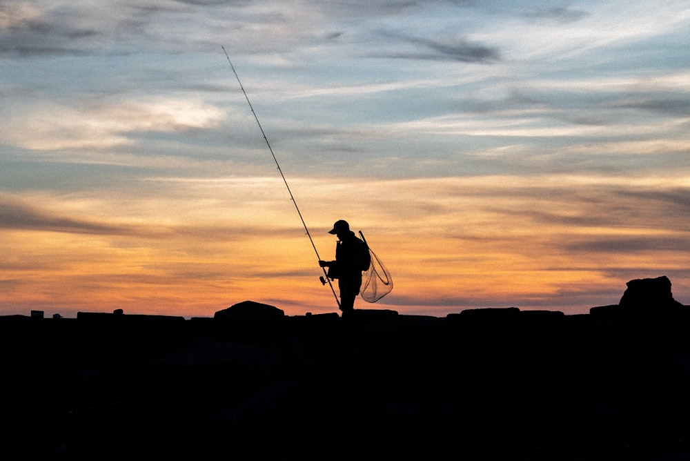 silhouette of man holding fishing rod during sunset