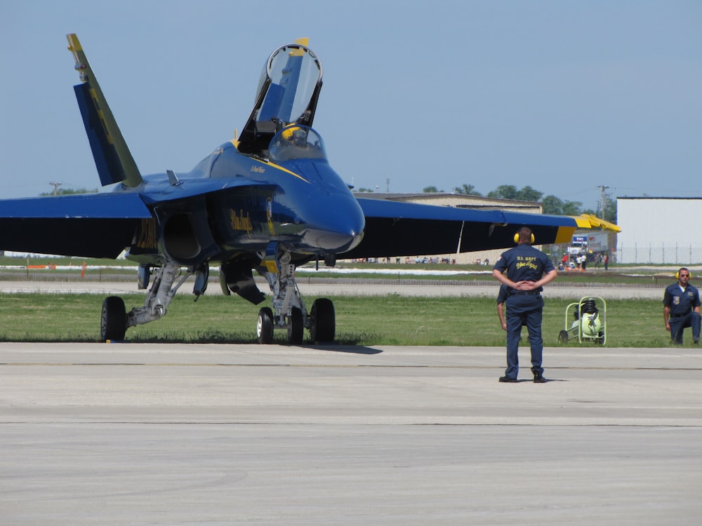man in yellow jacket and brown pants standing beside blue jet plane