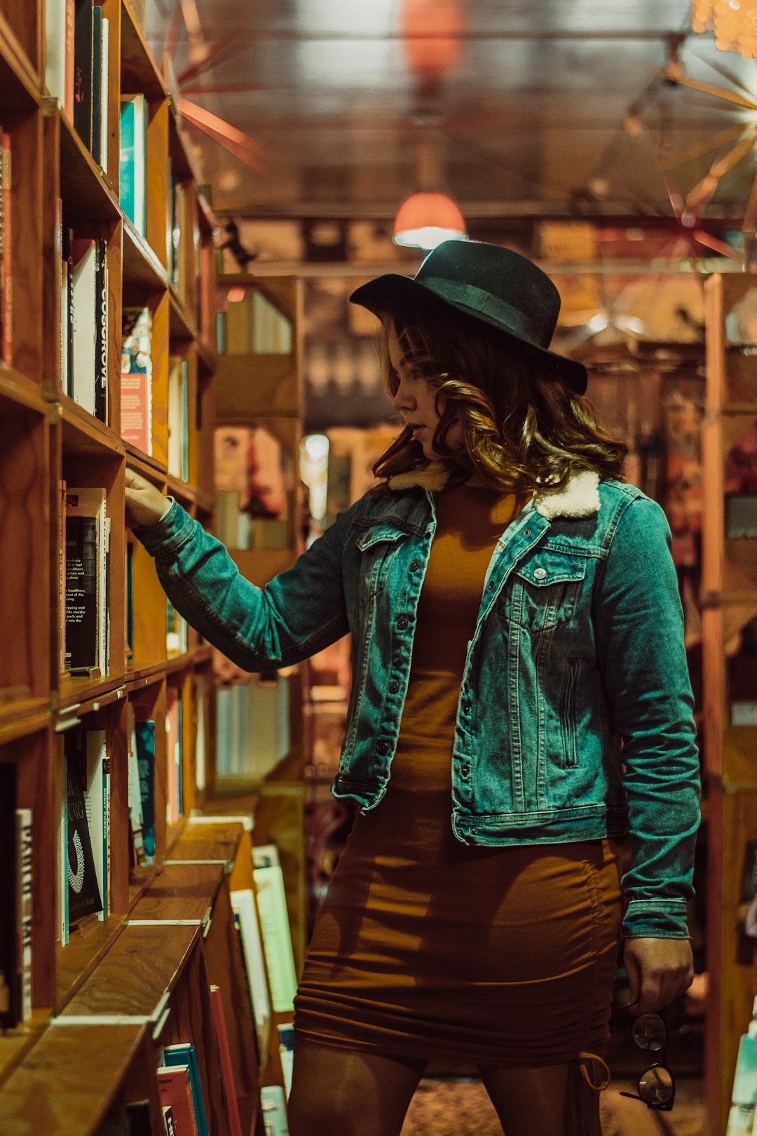 woman in blue denim jacket and black hat standing beside brown wooden shelf