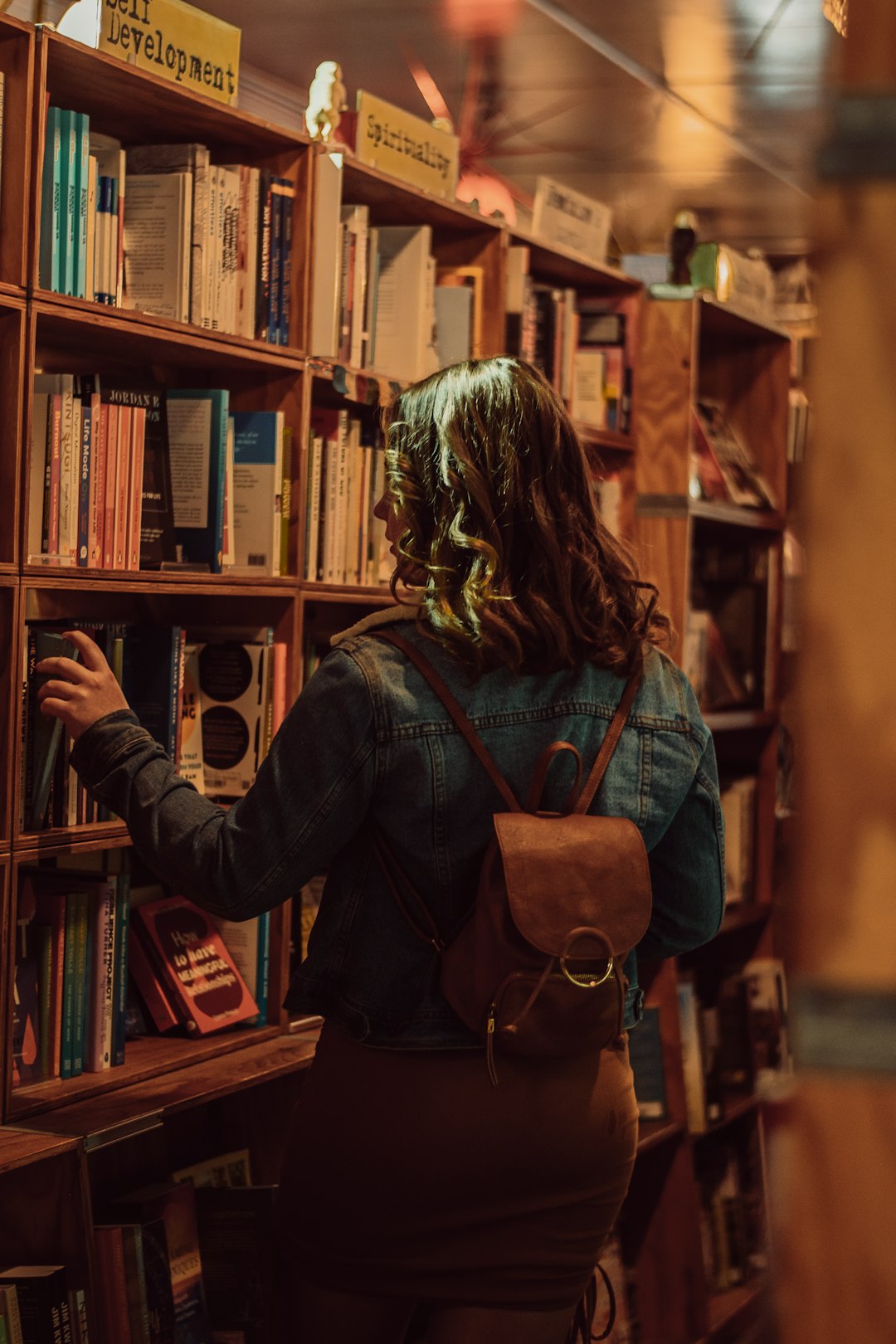 woman in blue denim jacket holding brown leather sling bag