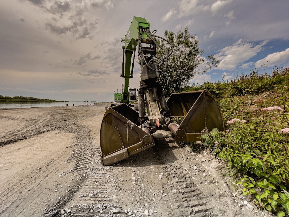 Équipement lourd vert et brun sur sable gris sous un ciel nuageux gris pendant la journée