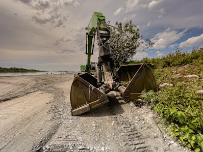 green and brown heavy equipment on gray sand under gray cloudy sky during daytime