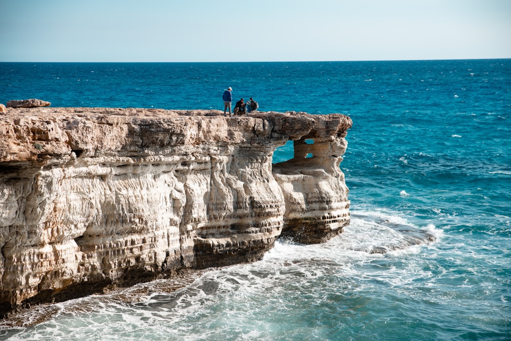 2 people standing on brown rock formation near body of water during daytime