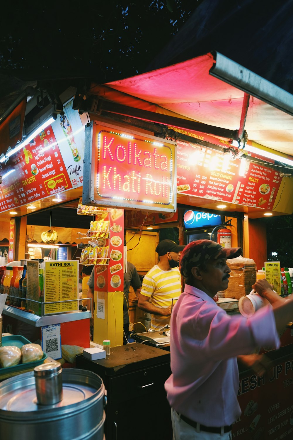 Mujer con camisa rosa de pie frente a un puesto de comida