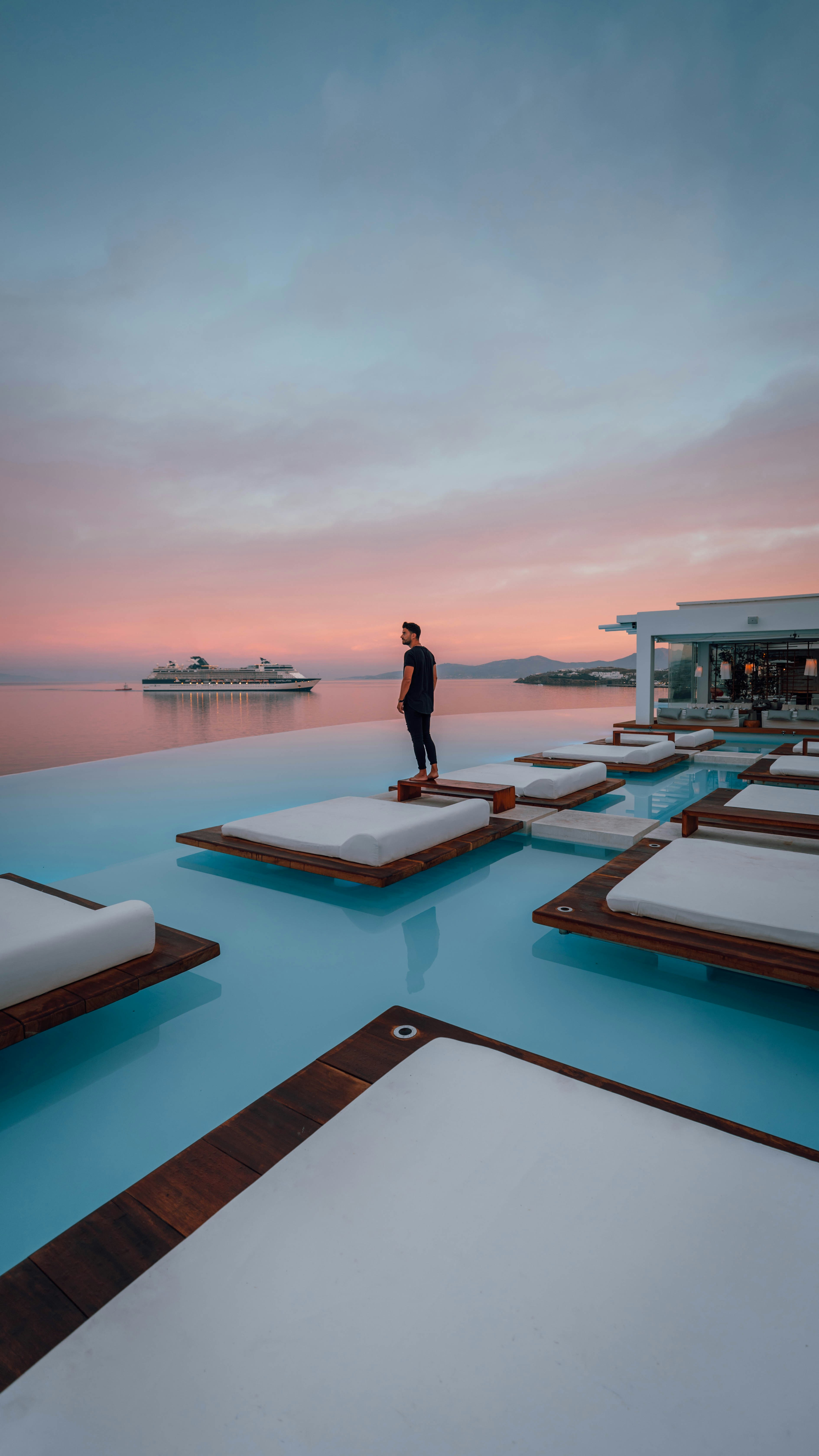 woman in black dress standing on white and brown pool near blue body of water during