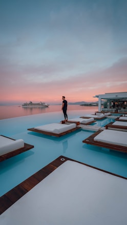 woman in black dress standing on white and brown pool near blue body of water during