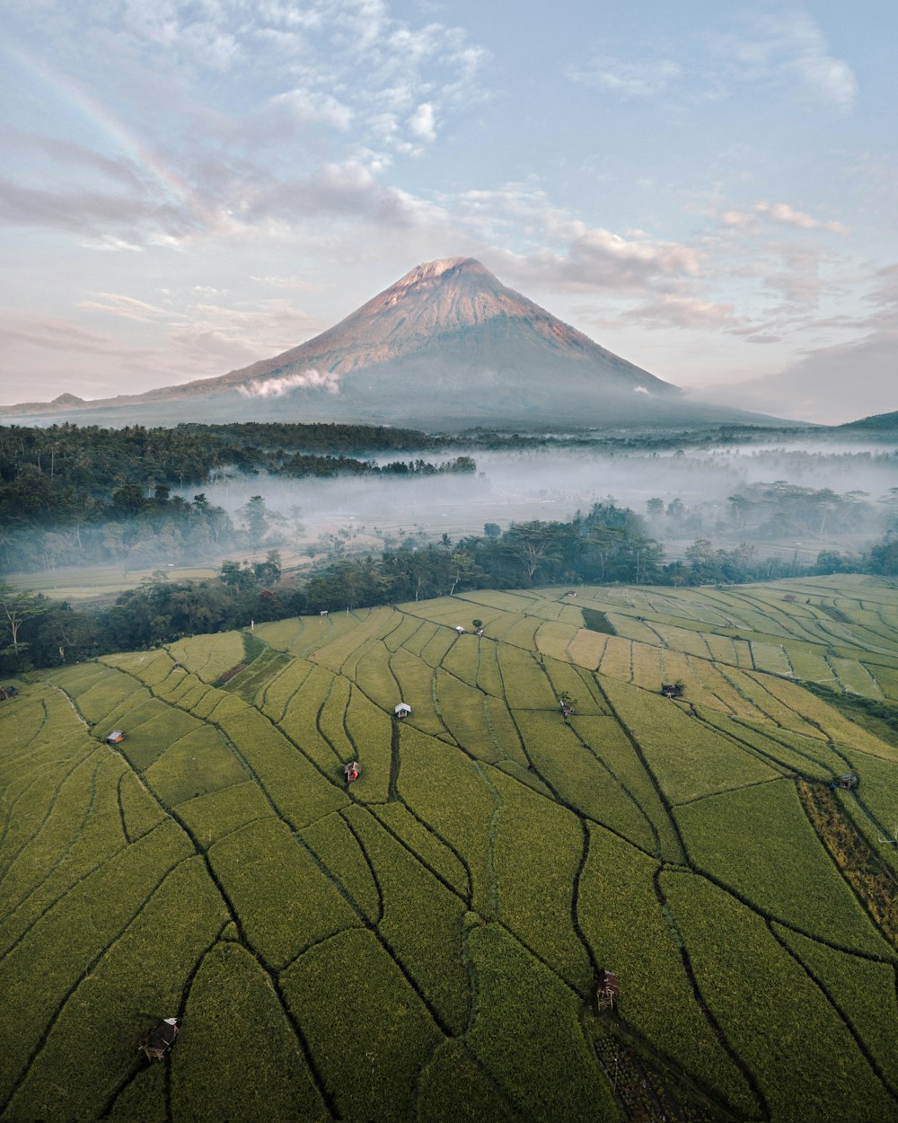 green grass field near mountain under white clouds during daytime