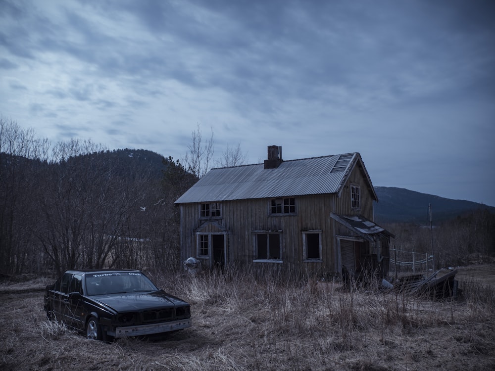 black car parked beside brown wooden house during daytime