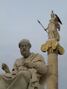 A modern marble statue of a philosopher with subtle golden particles floating around.