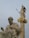 A detailed marble statue of an ancient philosopher seated, juxtaposed with a towering statue of a goddess holding a spear and shield on a column with ornate gold accents.