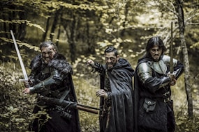 3 men in black leather jackets standing on brown wooden fence during daytime