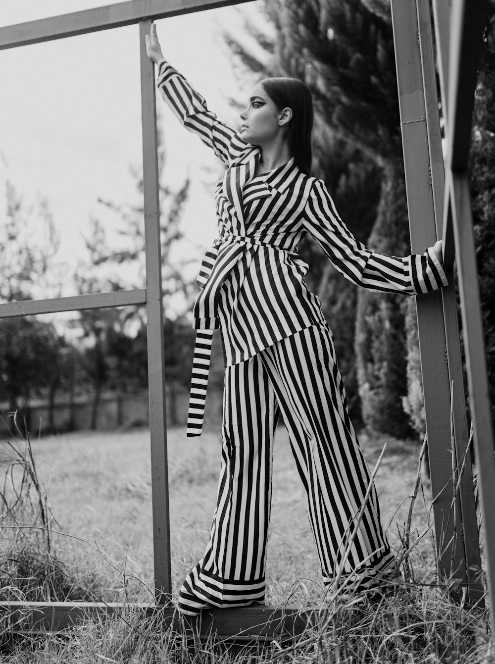 grayscale photo of woman in stripe dress standing near window