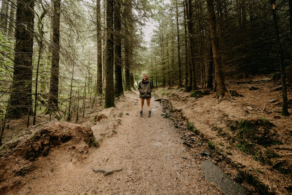 man in black t-shirt and black shorts walking on dirt road in between trees during