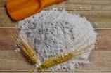 Close-up of freshly milled white rice flour spilling from a traditional wooden scoop.